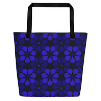 A tote bag with black handles features a vibrant, repeating pattern of abstract blue flowers on a dark background, creating a bold and modern look.
