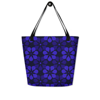 A tote bag with black handles features a vibrant, repeating pattern of abstract blue flowers on a dark background, creating a bold and modern look.