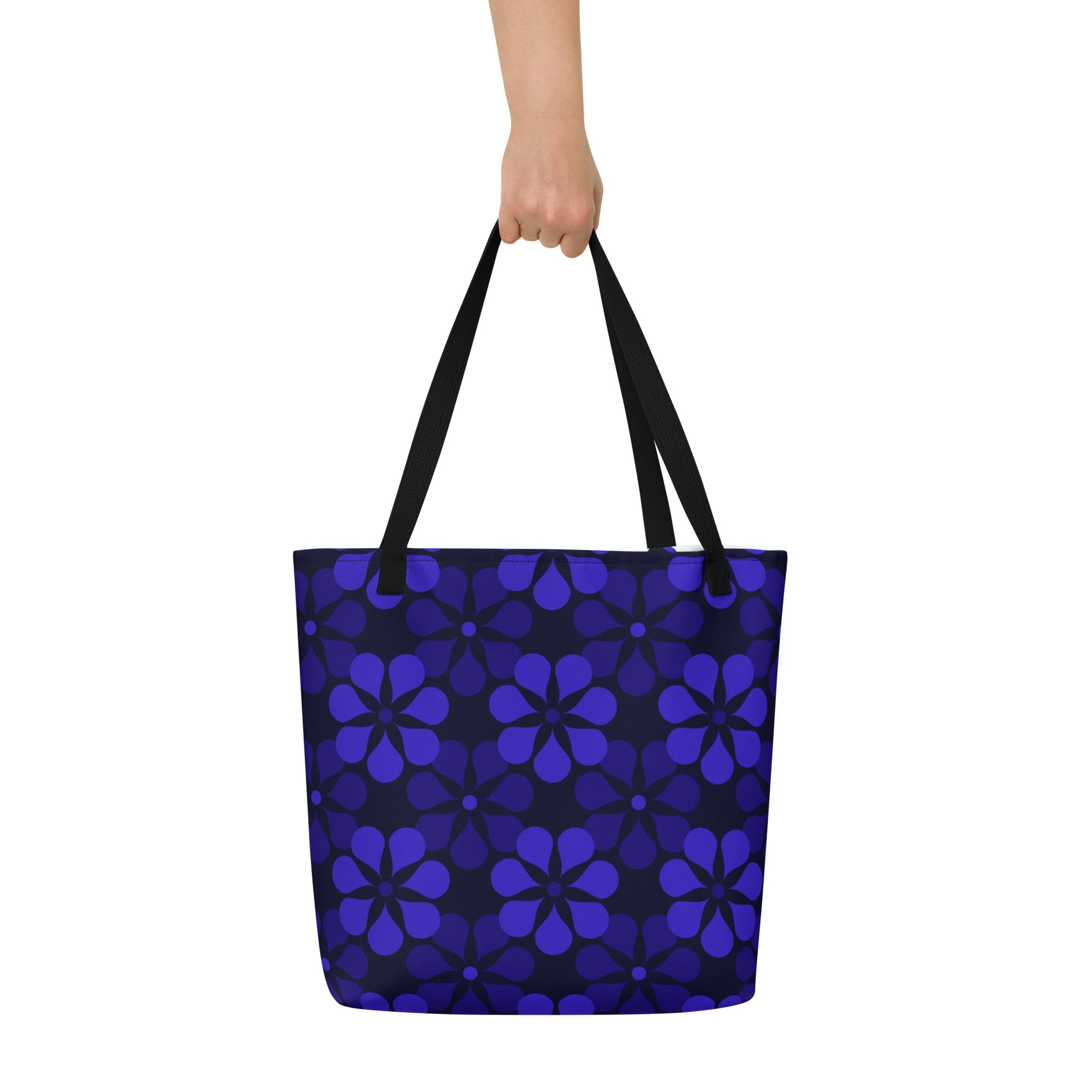 A tote bag with black handles features a vibrant, repeating pattern of abstract blue flowers on a dark background, creating a bold and modern look.