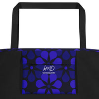 A tote bag with black handles features a vibrant, repeating pattern of abstract blue flowers on a dark background, creating a bold and modern look.