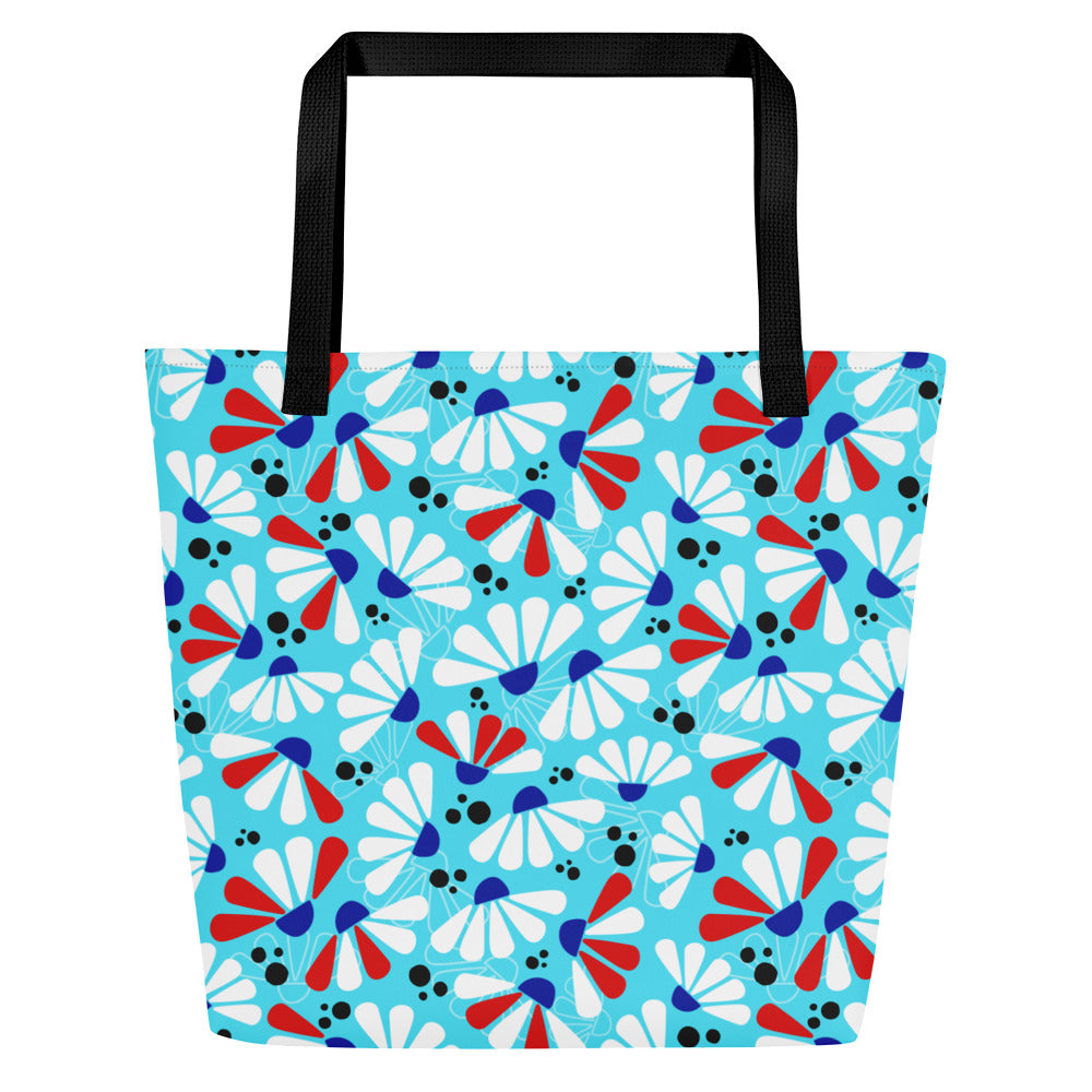 Tote bag with a vibrant pattern of abstract coneflower florals in white, red, and blue on a light blue background. Black handles contrast boldly.