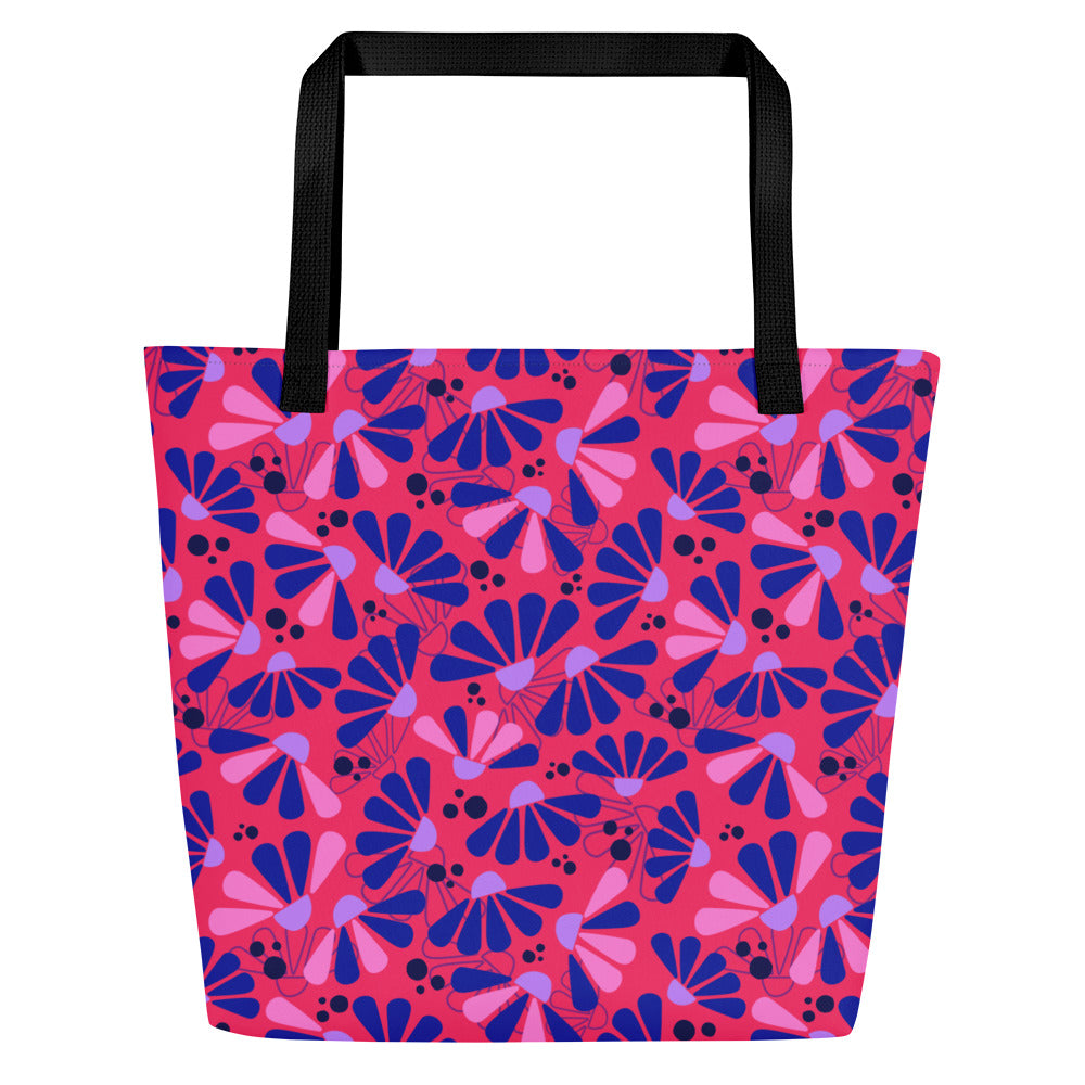 A vibrant tote bag with bold black handles features a colorful pattern of abstract coneflowers in blue, pink, and purple on a red background.