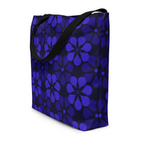 A tote bag with black handles features a vibrant, repeating pattern of abstract blue flowers on a dark background, creating a bold and modern look.