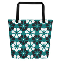 A tote bag with black handles features a vibrant, repeating pattern of abstract teal, white, and black flowers on a dark teal background, creating a bold and modern look.