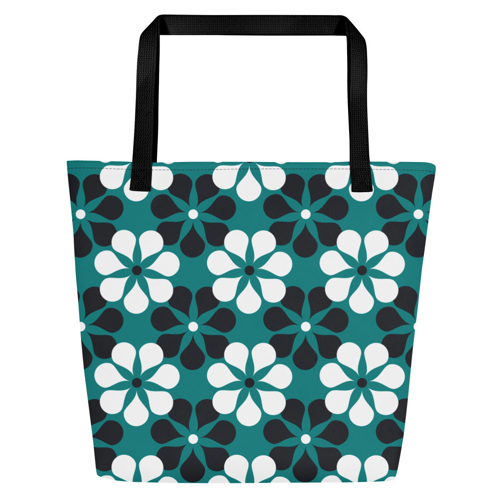A tote bag with black handles features a vibrant, repeating pattern of abstract teal, white, and black flowers on a dark teal background, creating a bold and modern look.